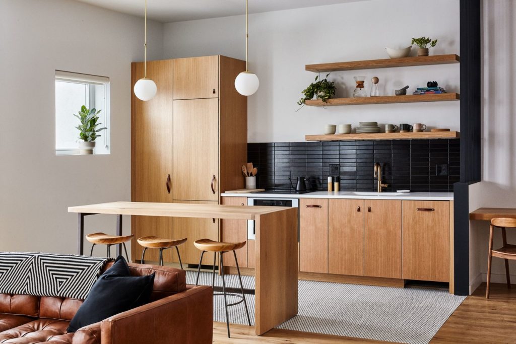 A white oak modern kitchen with white penny tile floors and matte black tile backsplash with two floating shelves and custom steel and wood island