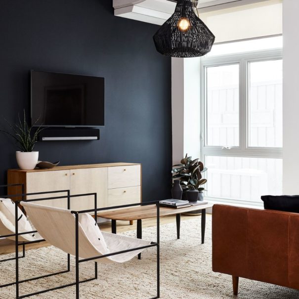 The Living room in the Baller Jawn at Lokal Hotel Fishtown with leather couch, two sling lounge chairs, a woven overhead light and locally handmade wooden coffee table and credenza under smart tv and sonos speaker