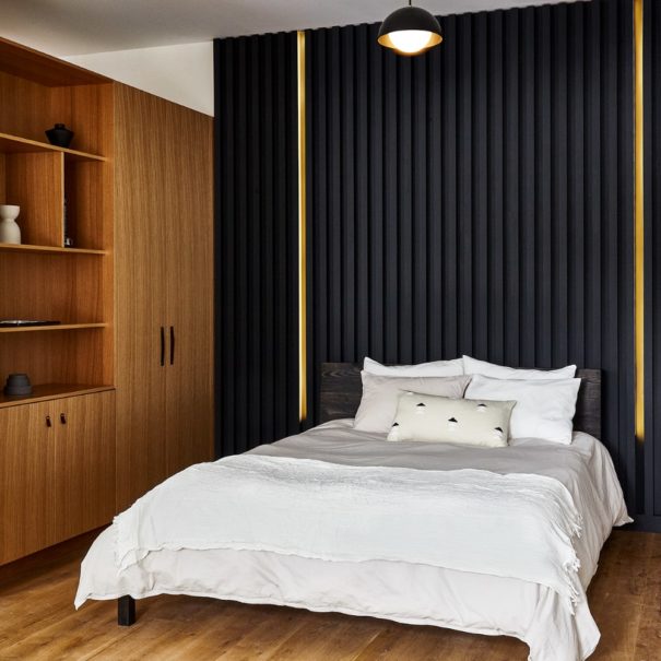 Queen bed with casper mattress and parachute linens with floor to ceiling black headboard with integrated led lighting and white oak shelving and wardrobe