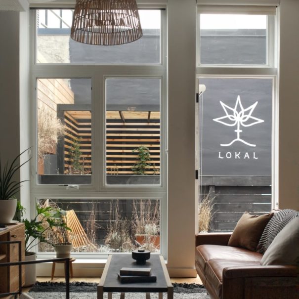 View of the Garden Jawn living room at Lokal Hotel Fishtown looking over the garden through the windows in the back of the property with seating, trellis and logo painted on the back wall