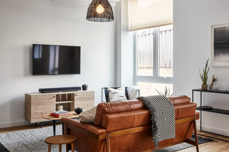 Living room in the Lokal Hotel Fishtown studio apartment room with leather couch area rug steel bar table and handmade bleached wood console underneath the smart tv with sonos soundbar
