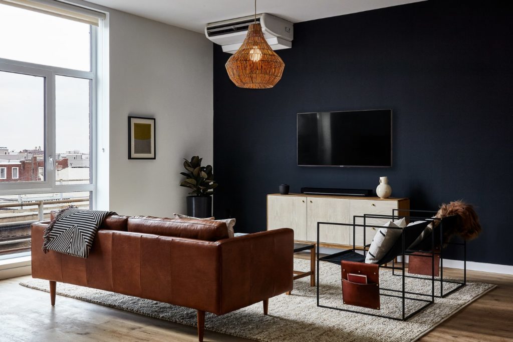 The living room at the Baller Jawn of Lokal Hotel Fishtown with leather couch 2 custom side chairs and coffee table and console handmade by local makers on an area rug with huge floor to ceiling windows overlooking center city philadelphia